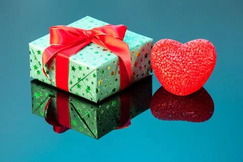 Single green gift box with red heart on blue reflective surface. Gift box wra Stock Photos