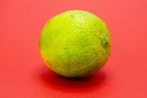 A single green lime sits on a red background. Stock Photos