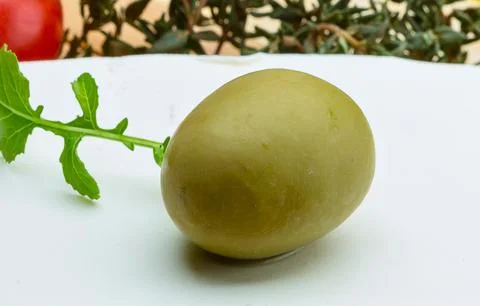 Single green olive with leafy stem on white surface Stock Photos