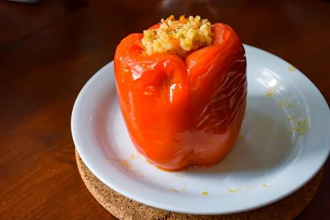 A single hot stuffed red bell pepper served on a white plate on a wooden table Stock Photos