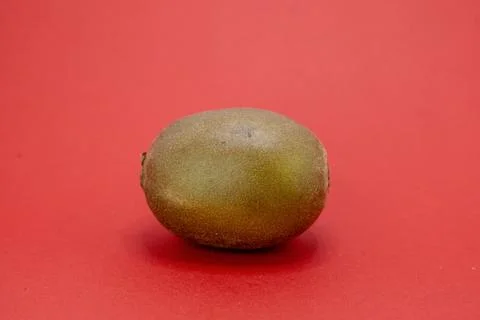 A single kiwi fruit sits on a red background. Stock Photos