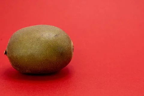 A single kiwi fruit sits on a red background. Fotos de archivo