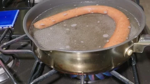 A Single Large Smoked Sausage Boiling in Water on a Kitchen Gas Stove Stock Footage 320030253