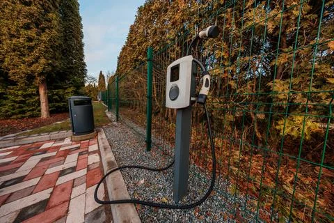 Single Level 2 EV charger by green fence in late afternoon light Stock Photos