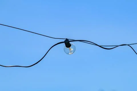Single light bulb hangs on black wire against clear blue sky. Wire bends Stock Photos
