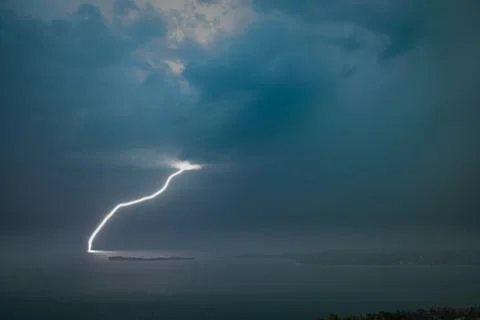 Single lightning bolt striking Lake Garda, Italy under a dark stormy sky Stock Photos