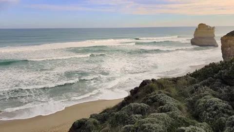Single limestone sea stack standing in heavy ocean surf viewed over coastal Stock Footage 345288169