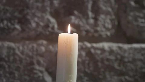 Single Lit White Candle Burning Against A Rough Stone Wall Stock Footage 343704414