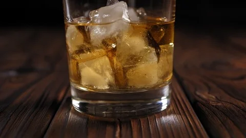 Single malt whiskey with ice cubes on wooden background. Close-up. Slow motion. Stock Footage 123708803
