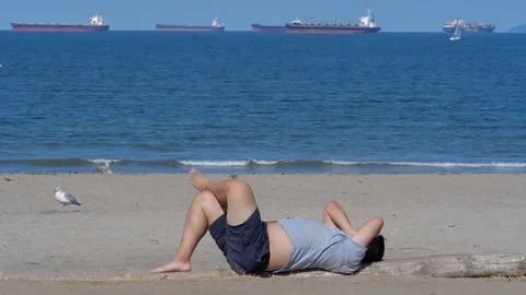 A single man dressed in T-short and shorts lying on a log taking the sun. Vidéo 158284217