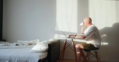 A single man sits at a table in his apartment and works using a laptop Stock Footage 302901383