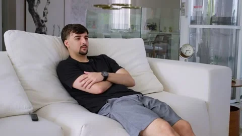 Single man sitting on the couch in the living room with his arms crossed. Stock Footage 247660832