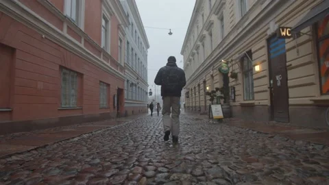 Single man walking down an empty, wet cobbled street in Helsinki, Finland Stock Footage 146290951