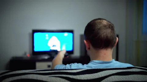 Single man watching TV in the evening sitting on the sofa, rear view Stock Footage 132882643