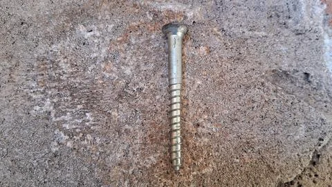 Single metal screw on stone background. Industrial fastener for construction and Stock Photos
