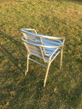 Single metallic chair casting shadow on grassy field Foto stock