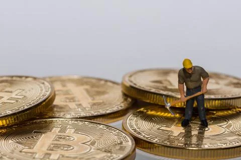 Single miner working on a stack of bitcoins crypto currency with gray Stock Photos