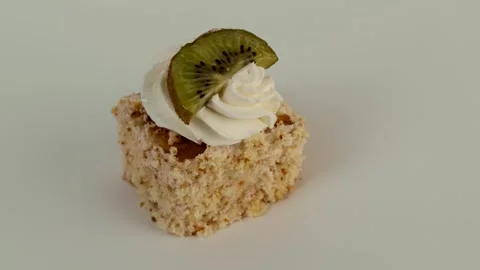 A single mini cake topped with piped whipped cream and a fresh kiwi slice stands Video stock 309637701