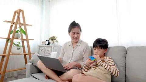Single mom using laptop for work from home and son sitting next to mom tryi.. Stock Footage 249452175
