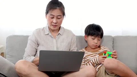 Single mom using laptop for work from home and son sitting next to mom tryi.. Stock Footage 249522192