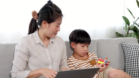 Single mom using laptop for work from home and looking son sitting next to .. Stock Footage 249522446