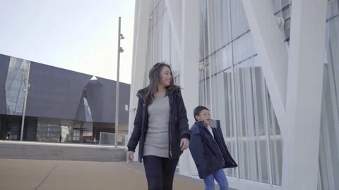 Single mother walks through the city while her son plays and jumps happily ar Stock Footage 149055253