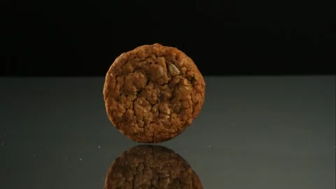 Single Oatmeal Cookie Rolling Across A Dark Reflective Stock Footage 326290432
