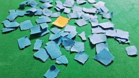 Single orange paper square surrounded by many torn blue pieces Stock Photos