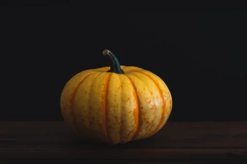 Single orange pumpkin on a dark brown table with black background. Stock Photos