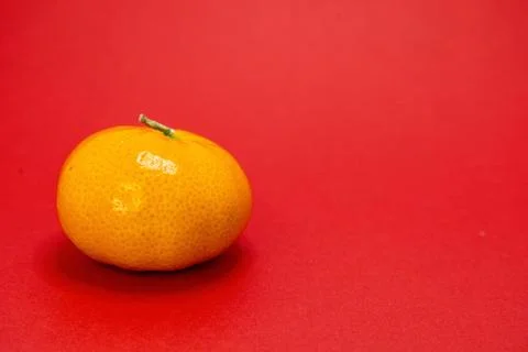 A single orange sits on a red background. Stock-Fotos