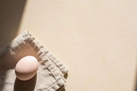 Single pale egg rests on a folded linen napkin with soft shadows and light Stock Photos