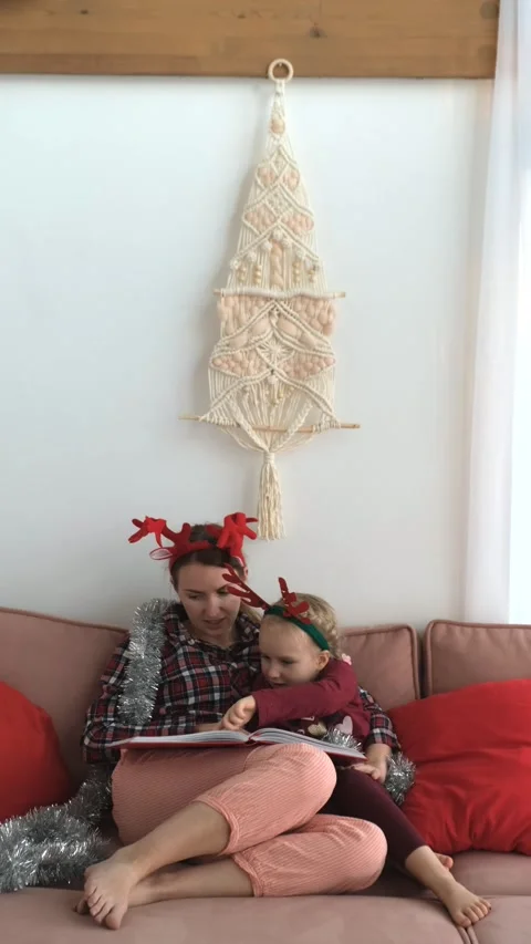 Single parent mom and her daughter reading book with Christmas tree wall decor Stock Footage 258374084