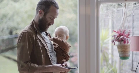 Single parent working from home on smart phone and holding baby Stock Footage 118618146