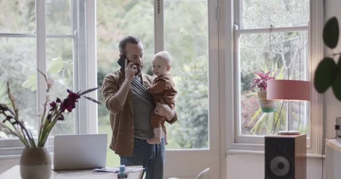 Single parent working from home on smart phone and holding baby Stock Footage 118621625