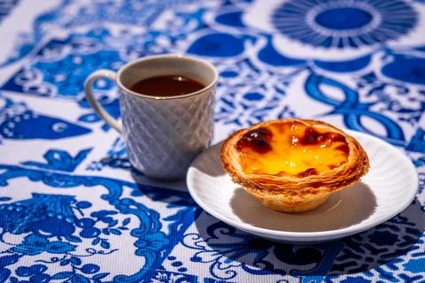 Single pastel de nata custard tart with coffee cup on blue tablecloth on sunny Stock Photos