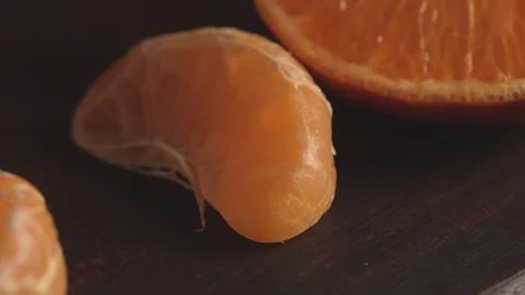 A single peeled mandarin orange segment rests on a dark wood surface Stock Photos