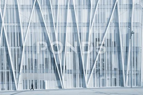 A single person walking in front of a modern business building. Stock Photos