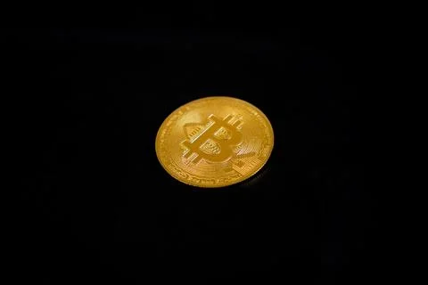 A single physical golden Bitcoin token coin centered on a solid black backg.. Stock Photos