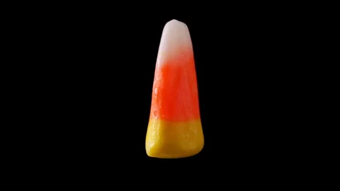 A single piece of candy corn is seen slowly rotating. The candy corn Stock Footage 116399770