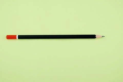 Single piece of sharpened black pencil lying over a light green paper Stock Photos