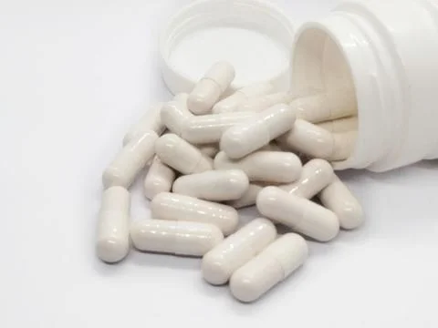 A single pill resting on a plain white background Stock Photos