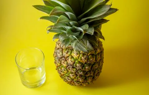 Single pineapple isolated on yellow background with empty glass. Stock Photos