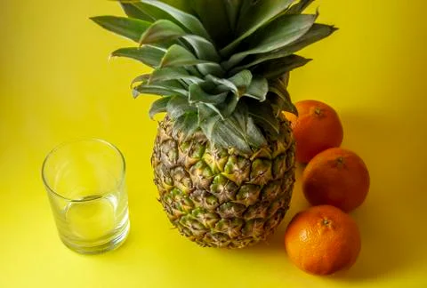 Single pineapple isolated on yellow background with empty glass and mandarin  Stock Photos