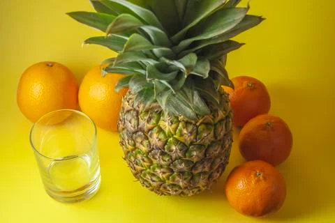 Single pineapple isolated on yellow background with empty glass and mandarin  Stock Photos