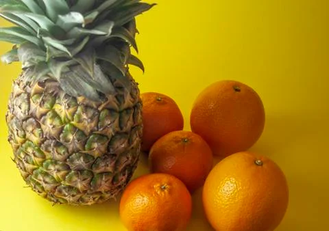 Single pineapple isolated on yellow background with oranges and mandarin oran Stock Photos