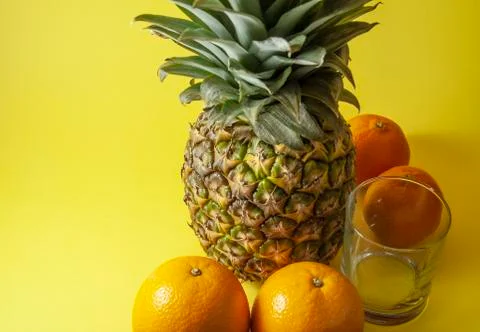 Single pineapple isolated on yellow background with empty glass and mandarin  Stock Photos