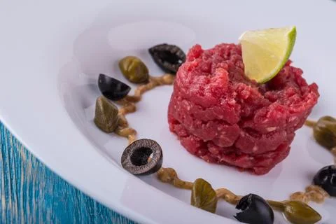 Single portion of tartar steak on white plate with lime Stock Photos