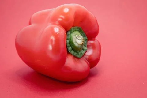 A single red bell pepper sits on a red surface, ready for cooking or decorati Stock Photos