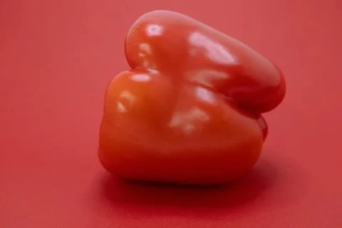 A single red bell pepper sits on a red surface. Stock Photos