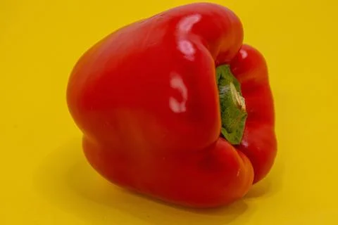 A single red bell pepper sits on a bright yellow background. Foto stock